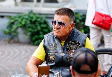 Villach, Avusturya - Eylül 05, 2025: Güneş gözlüklü ve deri yelekli kıdemli motosikletçi, Harley Treffen 'de Avrupa Bisiklet Haftası' nın keyfini çıkarıyor, canlı atmosferle çevrili