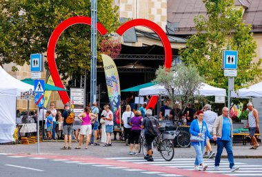 Villach, Avusturya - Eylül 05, 2025: Açık hava pazarı insanların tezgahlara göz attığı kalp şeklinde bir kemer içeriyor, canlı ve renkli bir topluluk ortamı yaratıyor