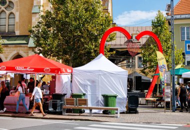 Villach, Avusturya - Eylül 05, 2025: Renkli çadırları ve kalp şeklinde kemeri olan açık hava pazarı, pitoresk bir kasaba meydanında canlı bir topluluk toplantısı sergiliyor.