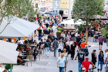 Villach, Avusturya - 05 Eylül 2025: İnsanların açık kafelerde yemek yediği kalabalık cadde, alışveriş ve canlı dekorasyonların keyfini çıkarıyor ve canlı bir ortam yaratıyor