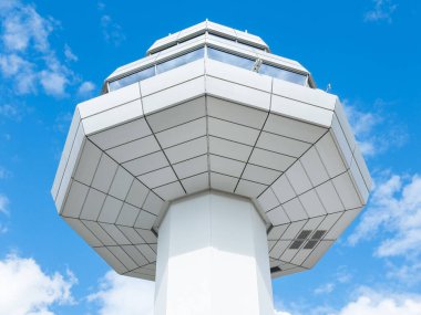 Klagenfurt, Avusturya - 25 Eylül 2025: Havaalanındaki kontrol kulesi, hava trafiği yönetimi ve havacılık sembolize eden mavi gökyüzü ve bulutlarla çevrili modern mimariye sahip
