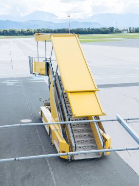 Klagenfurt, Avusturya - 25 Eylül 2025: Sarı tahta merdivenler havalimanı pistinde dağlar ve arka planda açık gökyüzü ile yer almaktadır