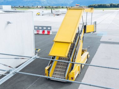 Klagenfurt, Avusturya - 25 Eylül 2025: Sarı tahta merdivenler havaalanının yanına yerleştiriliyor, pistteki uçağa erişim sağlanıyor, seyahat ve ulaşımı vurguluyor