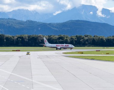 Klagenfurt, Avusturya - 25 Eylül 2025: Malta Hava Yolları çarpıcı dağ manzarası ile pistte taksicilik yapıyor, hava yolculuğunun ve maceranın özünü yakalıyor