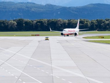 Klagenfurt, Avusturya - 25 Eylül 2025: Havaalanında, dağlarla ve mavi gökyüzüyle havalimanında taksicilik yapan uçak, manzaralı bir seyahat atmosferi yaratıyor