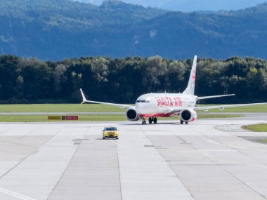 Klagenfurt, Avusturya - 25 Eylül 2025: Malaya Hava Yolları, havaalanı operasyonları ve havacılık dinamiklerini gösteren servis aracıyla pistte taksicilik yapıyor