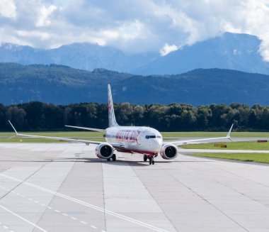 Klagenfurt, Avusturya - 25 Eylül 2025: Arka planda güzel dağlar, seyahat ve havacılık atmosferini ön plana çıkaran uçak havaalanında hareket ediyor