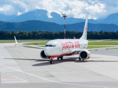 Klagenfurt, Avusturya - 25 Eylül 2025: Malta Air Boeing 737, güzel dağları ve arka planda açık gökyüzü bulunan havaalanında pistte taksicilik yapıyor