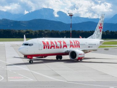 Klagenfurt, Avusturya - 25 Eylül 2025: Malta Air Boeing 737 çarpıcı dağ zeminiyle havaalanının pistinde taksicilik yapıyor