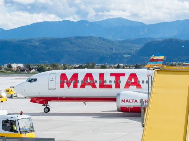 Klagenfurt, Avusturya - 25 Eylül 2025: Malta Havayolları Boeing 737 arka planda güzel bir dağ manzarası ve parlak gökyüzü ile havaalanında park edilmiştir.