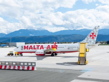 Klagenfurt, Avusturya - 25 Eylül 2025: Malta Hava Yolları uçakları, seyahat ve havacılığın altını çizen manzaralı bir dağ zeminiyle havalimanında konuşlandırıldı