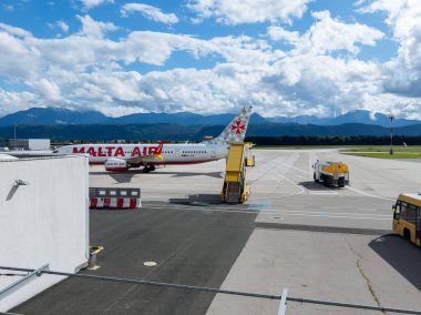 Klagenfurt, Avusturya - 25 Eylül 2025: Malta Hava Yolları uçakları, bir dağ zeminine ve açık gökyüzüne karşı, kalkış merdivenleriyle havalimanında konuşlandırıldı