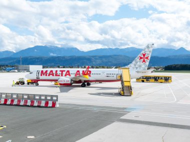Klagenfurt, Avusturya - 25 Eylül 2025: Malta Hava Yolları uçakları arka planda çarpıcı dağ manzaralı havaalanı terminalinde konuşlandırıldı