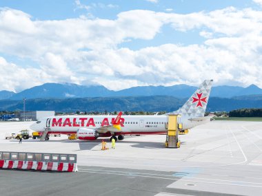 Klagenfurt, Avusturya - 25 Eylül 2025: Malta Hava Yolları uçakları çarpıcı bir dağ zeminiyle havaalanı terminalinde konuşlandırıldı, seyahat ve havacılık dinamikleri vurgulandı