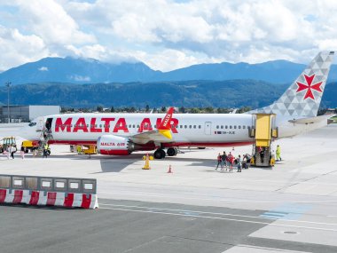 Klagenfurt, Avusturya - 25 Eylül 2025: Havalimanı terminalinde yolcu alımı, canlı markalaşma ve manzaralı dağ manzaralı Malta Air uçağı