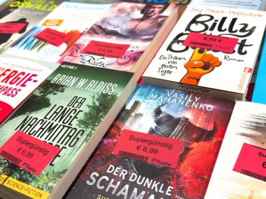 Villach, Avusturya - 17 Eylül 2025: Canlı bir kitapçıda bir masada sergilenen fiyat etiketli kitap kapaklarının canlı çeşitliliği