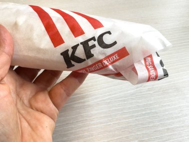 Villach, Avusturya - 17 Eylül 2025: Hand, KFC Zinger Deluxe sandviçini kırmızı çizgili ve logolu tanınabilir kağıda sardı