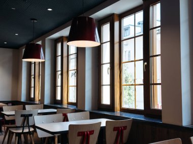 Villach, Avusturya - 17 Eylül 2025: Modern kafe büyük pencereler, kolye ışıkları ve minimalist ahşap masalar sergileyerek misafirler için sıcak bir ortam yaratıyor