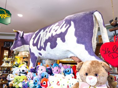 Villach, Avusturya - 17 Eylül 2025: Büyük Milka inek pelüş oyuncağı neşeli bir hediye dükkanında çeşitli renkli doldurulmuş hayvanlar arasında gururla duruyor