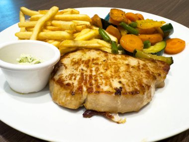 Kızarmış domuz pirzolası ve beyaz tabakta karışık sebze..