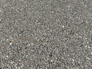 Asfalt yüzeyinde çakıl taşları ve gün ışığında küçük taşlar var..