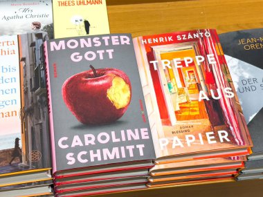 Villach, Austria - September 28, 2025: Vibrant book covers of 'Monster Gott' and 'Treppen aus Papier' arranged neatly on a wooden shelf in a cozy bookstore