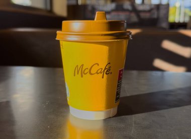 Ljubljana, Slovenia - October 02, 2025: McCafe coffee cup is placed on a shiny table in a warm cafe environment, highlighting its bright yellow design