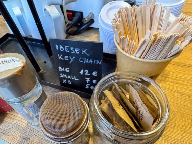 Ljubljana, Slovenia - October 02, 2025: Obesek key chain pricing displayed alongside wooden stirrers and jars of sugar and cinnamon on a wooden counter