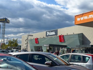 Ljubljana, Slovenia - October 02, 2025: Exterior of Prima shopping center with modern design, parked cars in foreground, and dramatic clouds above