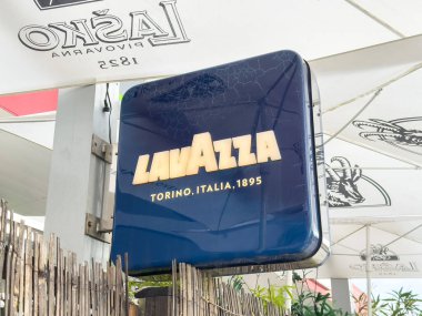 Ljubljana, Slovenia - October 02, 2025: Lavazza coffee sign shines brightly in outdoor cafe, surrounded by umbrellas and plants, creating a welcoming atmosphere
