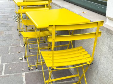 Bright yellow outdoor cafe chairs and table on a stone-paved street.