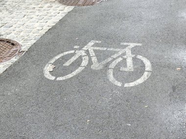 Asfalt yolda kaldırım taşı ve rögar kapaklı bisiklet sembolü.