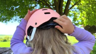 Küçük bir kız, eliyle kafasına pembe bir koruyucu kask takar ve sıkar. Miğfer boyutu, yaz sporları. Yüksek kalite