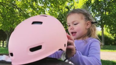 Küçük tatlı bir kız kafasına pembe bir kask takıyor. Paten kaymayı ya da bisiklete binmeyi öğreniyor. Yüksek kalite fotoğraf