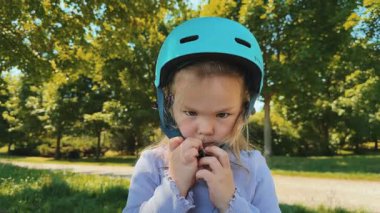 Küçük bir kız mavi koruyucu kaskını açar ve kaskını kafasından çıkarır. Eğitim sona erdi. Yazın bisiklet sürmek. Yüksek kalite 4k görüntü
