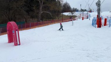 Pembe miğferli bir kız kayak pistinde çocuklarla piste çıkıyor ve kapıya doğru gidiyor. Yüksek kalite 4k görüntü