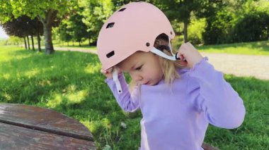 Küçük sevimli bir kız kafasına pembe bir kask takar ve onu takmaya çalışır. Paten kaymayı ya da bisiklete binmeyi öğreniyor. Yüksek kalite 4k görüntü