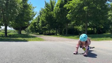 Kız paten kayıyor ve düşüyor. Dizlere ve dirseklere koruma ile düzgün bir şekilde düşmek. Başında kask var. Yüksek kalite 4k görüntü