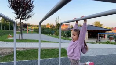 Küçük kız oyun parkındaki düzensiz barlarda jimnastik yapıyor. Açık hava eğitimi. Yüksek kalite 4k görüntü