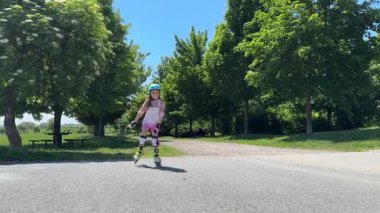 Kız yol boyunca koruyucu ekipman ve kaskla paten sürüyor. Yaz eğlencesi, spor, tatiller, okul çocuklarının hobileri. Yüksek kalite 4k görüntü