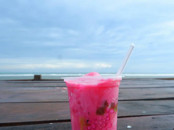 Es Podeng or Pink drink on a wooden table with Beach Background, Indonesia