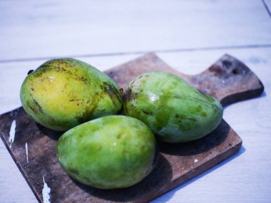 Three Arumanis mangoes on a wooden cutting board 