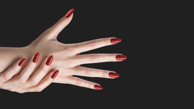 Tırnakları gri arka planda kırmızı parıltılı manikürlü genç bir kadının elleri.