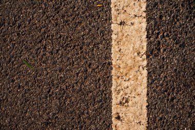 Pürüzlü asfalt üzerinde yıpranmış beyaz bir yol işaretinin detaylı bir yakın çekimi. Aşınmış boyalar ve desenli kaldırımlar kentsel bozulma ve ulaşım temalarını ön plana çıkararak, arka plan, altyapı ve seyahat ile ilgili görseller için ideal hale getiriyor..