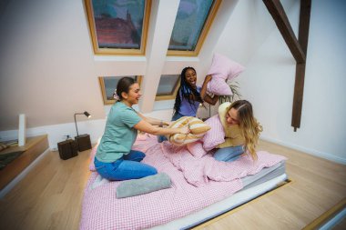 Çok ırklı genç kızlar yastık savaşı yapıyor evde pijama partisi veriyor, kızlar gecesi.