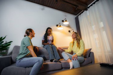 Neşeli çok ırklı bayan arkadaşlar evde birlikte vakit geçiriyorlar, gülüyorlar ve konuşuyorlar.