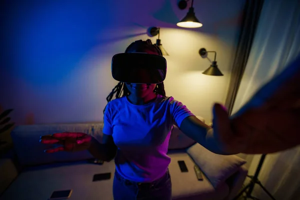 Excited girl wearing virtual reality headset in neon light trying to touch what she sees