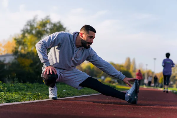 Koşu pistinde koşudan önce ya da sonra esneme hareketleri yapan bir adam. Güneşli bir gün, koşmak için mükemmel.