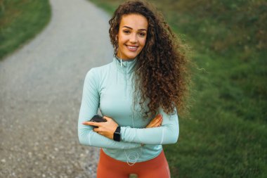 Bir kız elinde akıllı bir telefonla gülümsüyor, müzik dinliyor ve akıllı saatini gösteriyor..