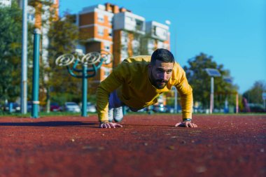 Parkta spor yapan erkek sporcu şınav çekiyor ve vücudunun üst kısmına odaklanıyor.